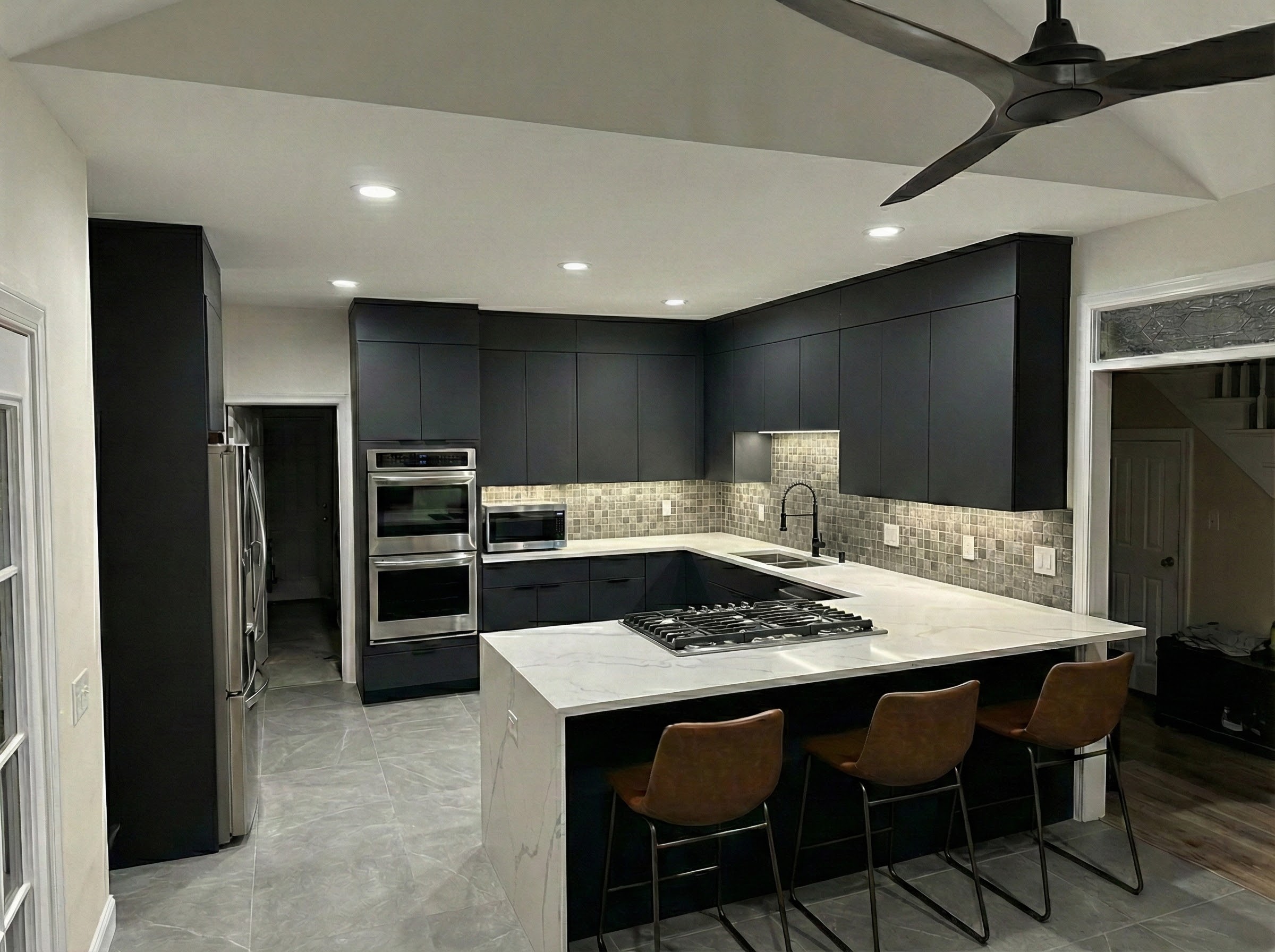 Completed kitchen renovation with matte dark cabinetry, marble-look waterfall island, stainless appliances and tile backsplash